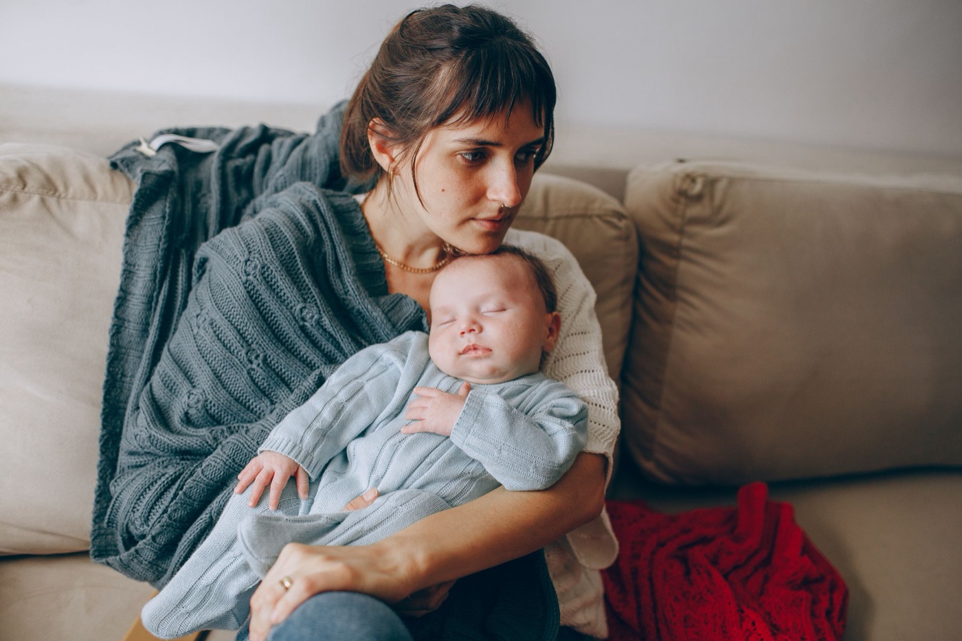 Mama po porodzie odpoczywa na kanapie w domu, owinięta kocem, z noworodkiem na rękach