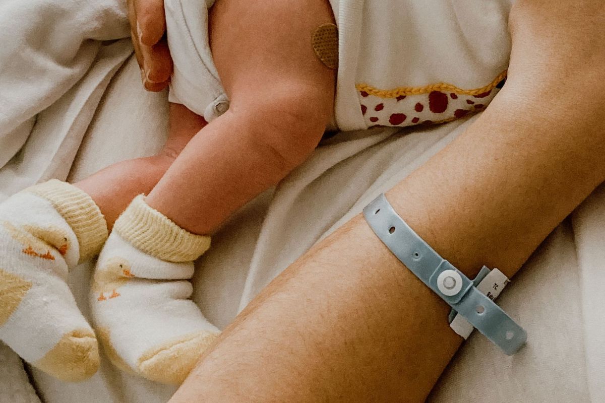Nóżki noworodka w skarpetkach i body obok ręki mamy z bransoletką szpitalną